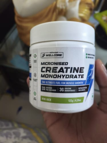 A customer holds a white tub of Wellcore Micronised Creatine Monohydrate, showing the Kiwi Kick flavor label.