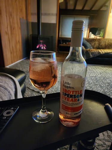 Reviewer's bottle of Rosé wine from the Fan Favourites pack and a glass with ice on a tray in a cozy living room.