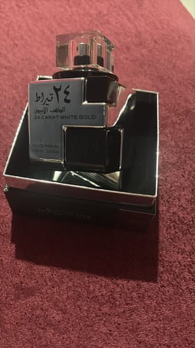 Cliente mostrando el perfume Lattafa 24 Carat White Gold en su elegante caja abierta sobre una superficie de tela.