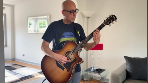 Reviewer wearing the black Statement Made Ukraine t-shirt while playing an acoustic guitar indoors.