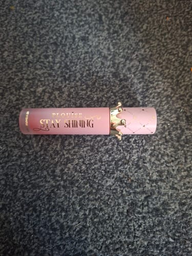 Customer's P.Louise Stay Shining Crown Lip Oil in its pink tube with a gold crown cap, lying on a dark textured surface.