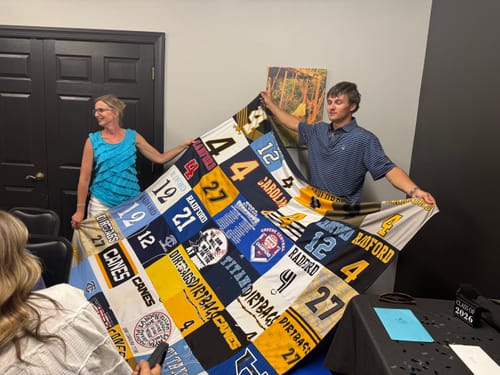 Customer and another person holding up a large, colorful Project Repat T-Shirt Quilt made from sports jerseys.