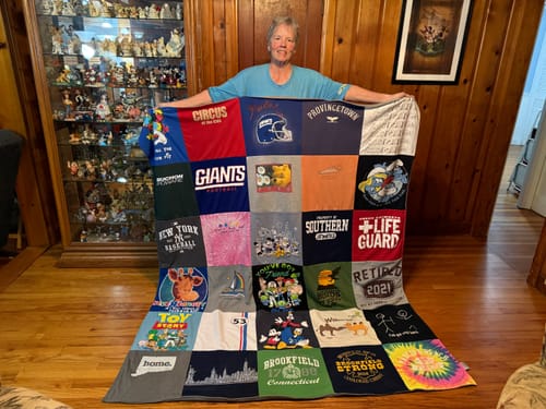 Reviewer proudly holding her large, colorful Project Repat T-Shirt Quilt made from many different shirts.