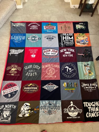 A customer's large T-shirt quilt, made from many colorful graphic tees, spread out flat on a floor.