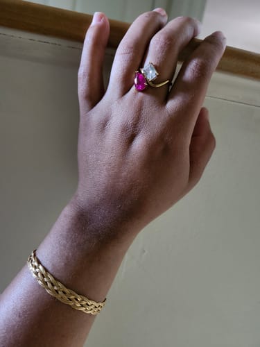 Customer's hand wearing the Navae Birthstone Ring with a pink pear-cut stone and a clear radiant-cut stone.