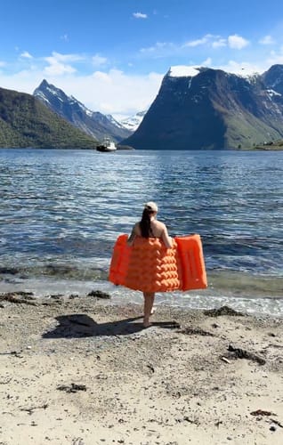 Hiker carrying Adventure Mat by a mountain lake