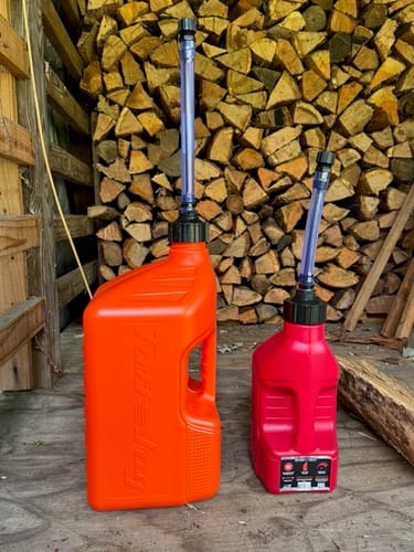 Reviewer's red 1.25 Gallon Tuff Jug shown for scale next to a larger orange Tuff Jug in front of a woodpile.