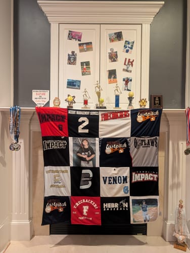 Customer's T-Shirt Quilt made of softball jerseys, draped over a fireplace with trophies and photos in the background.