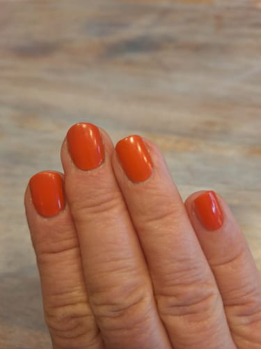 Nahaufnahme der Hand einer Kundin, die die glänzenden, rot-orangen "Red Stilettos" UV-Gel-Folien auf kurzen Nägeln trägt.