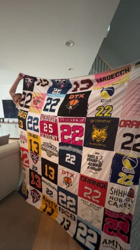 Reviewer holding up their large Project Repat T-Shirt Quilt made from colorful basketball jerseys.