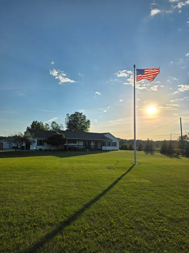 Customer's Heavy Duty American Nylon Flag waving on a tall flagpole in a yard at sunset.