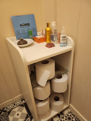 Client montrant plusieurs rouleaux de papier toilette compact stockés dans un meuble de salle de bain.