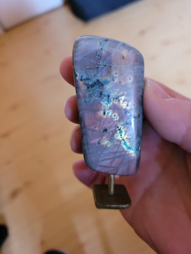 Client tenant sa labradorite sur socle, qui présente des reflets irisés violets et bleus.