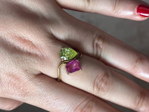Customer's hand showing the Navae Birthstone Ring with a pear-cut green stone and a radiant-cut pink stone.