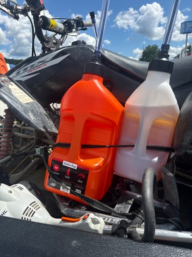 Reviewer's orange and white 5 Gallon Jugs strapped to the back of an ATV, ready for use outdoors.