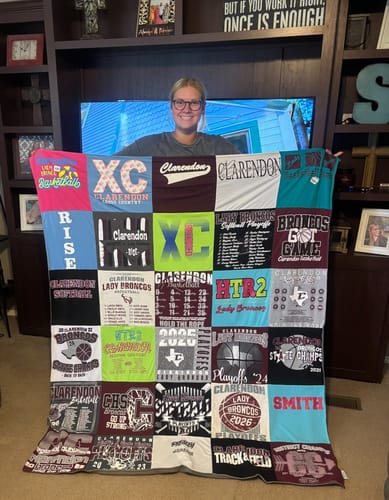 A smiling reviewer holds up their large Project Repat T-Shirt Quilt, made from many colorful sports t-shirts.