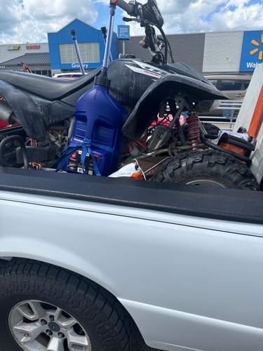 Customer's blue 5 Gallon Auto Stop Jug strapped in the back of a truck next to an ATV.