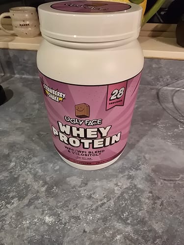 Customer's white tub of UGLYFACE® Strawberry Shake Whey Protein sitting on a kitchen counter.