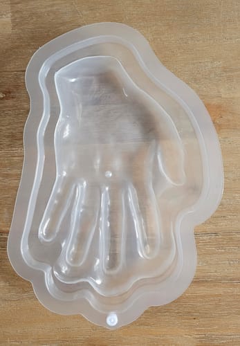 Kunde zeigt die Wackelpudding-Form in Gestalt einer Hand aus transparentem Kunststoff auf einer Holzoberfläche.