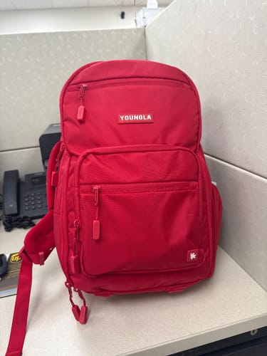Reviewer's bright red 730 Expedition Backpack standing upright on a desk in an office setting.