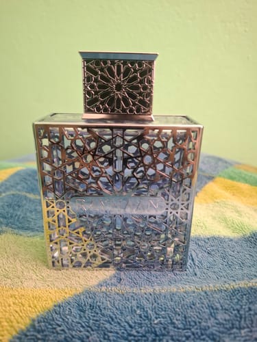 Reseñador muestra el perfume Rayhaan Aquatica en su frasco cuadrado con una intrincada celosía plateada.