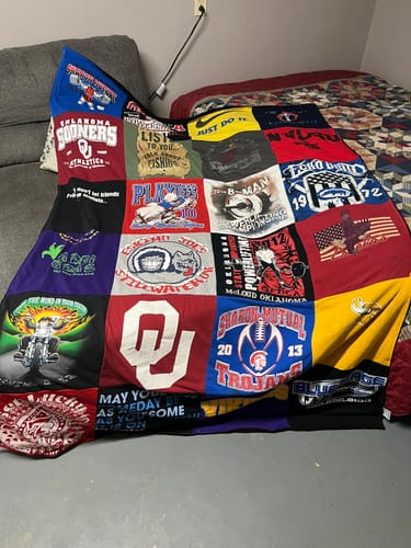 Customer's colorful Project Repat T-Shirt Quilt made from various graphic tees, draped over a couch and bed in a room.