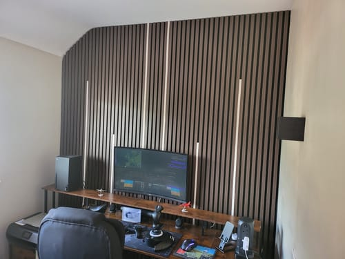 Customer's acoustic slatted wall panels installed behind a computer desk with vertical white LED lights turned on between the slats.