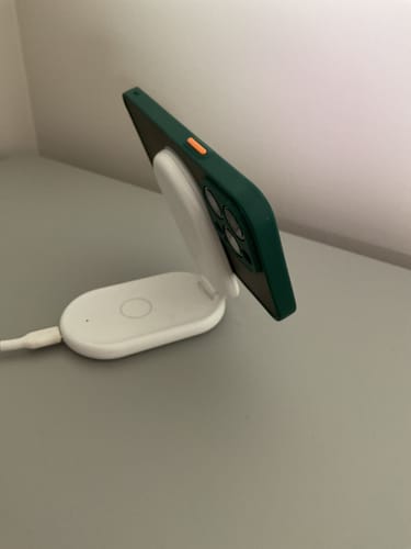 Customer's iPhone in a green MagSafe case charging on an angled white wireless charger on a desk.