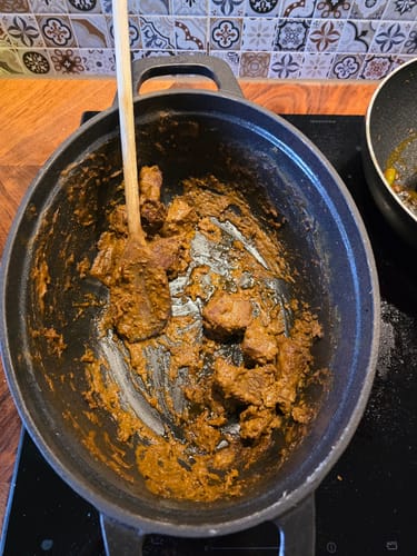 Klant roert in de dikke Rendang, gemaakt met de Rendang Bomb, in een zwarte stoofpan.