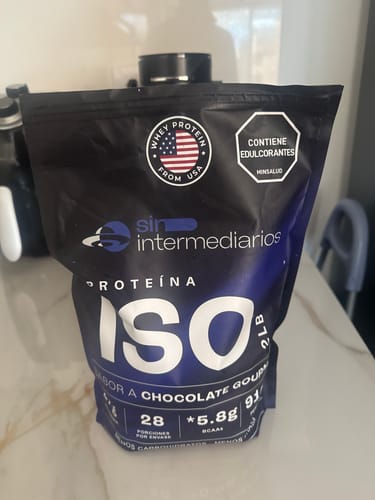 Un reseñador muestra la bolsa negra de Proteína Aislada ISO de chocolate sobre un mostrador de cocina.