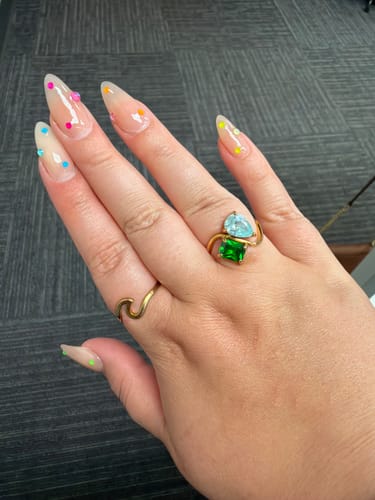 Customer's hand wearing the gold Navae Birthstone Ring with a light blue and green stone.