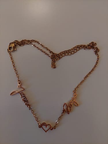 Ein Kunde zeigt seine personalisierte, roségoldfarbene Halskette mit zwei Namen und einem Herz, die auf einem Tisch in Herzform ausgelegt ist.
