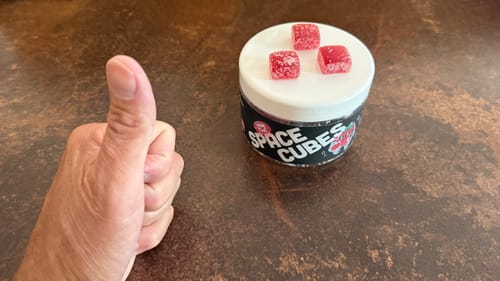 Kunde zeigt Daumen hoch neben der Dose Space Cubes mit drei roten Würfeln auf dem Deckel.