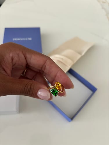 Customer holding the Navae Birthstone Ring with green and yellow stones above its blue jewelry box.