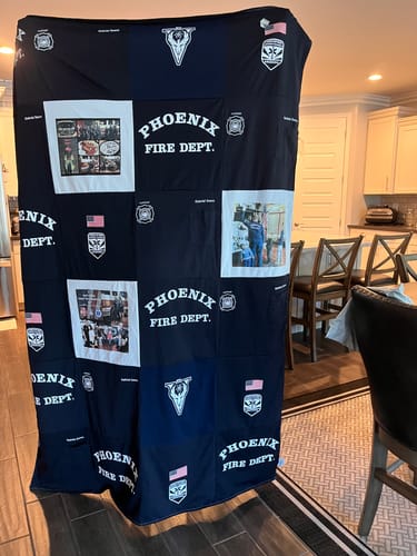 Customer's Project Repat T-Shirt Quilt made from navy Phoenix Fire Dept. shirts and photos, held up for display in a home.