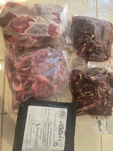 Customer's order showing several vacuum-sealed packages of Halal Goat Cubes-Gosht and other meats on a tile surface.