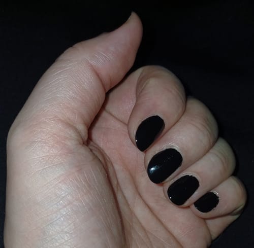 Nahaufnahme einer Kundenhand mit glänzenden, schwarzen 'Midnight Waltz' UV Gel Nail Wraps auf kurzen Nägeln.