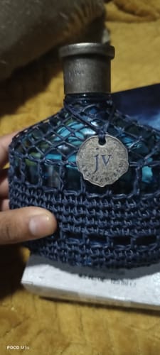 Cliente mostrando el frasco del perfume John Varvatos Artisan Blu con su cubierta tejida azul.