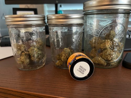 Customer's MAC THCA Flower buds displayed in three different-sized glass jars on a wooden desk.