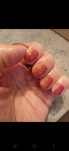 Nahaufnahme der Hand einer Kundin mit manikürten Nägeln, die die glänzenden, roten Burning Lava UV-Gel-Folien trägt.