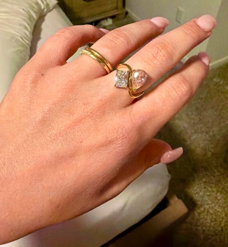 Customer's hand wearing the shiny Navae Birthstone Ring, showing the pear-cut pink and radiant-cut clear stones.