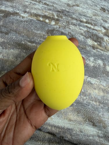 Customer holding the yellow Blem Clitoral Massager in their hand against a textured grey background.