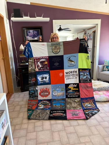 Reviewer holding up her large, custom Project Repat T-Shirt Quilt made from different t-shirts.