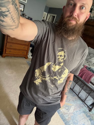 Reviewer showing the fit of the grey Lincoln Guitar T-Shirt in a selfie taken in a bedroom.