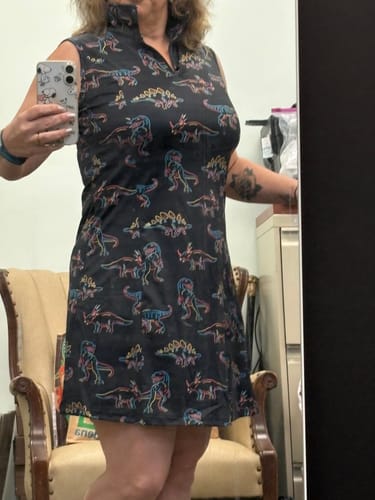Reviewer taking a mirror selfie in the black sleeveless golf dress with a colorful dinosaur print.