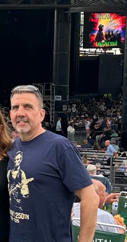 Reviewer wearing the navy blue Lincoln 250 T-Shirt with a graphic at an outdoor concert.