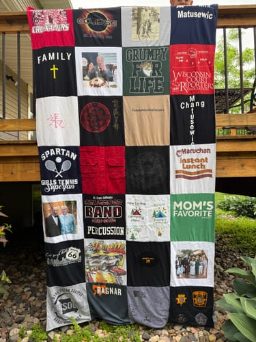 Customer holding up their large, custom Project Repat T-Shirt Quilt, made of many colorful t-shirts.