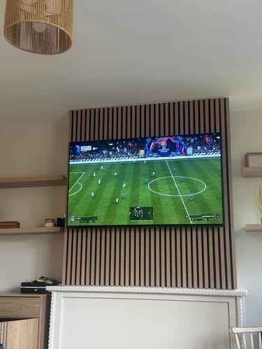 Customer's living room with light wood Acoustic Slatted Wall Panels installed as a feature wall behind a mounted television.