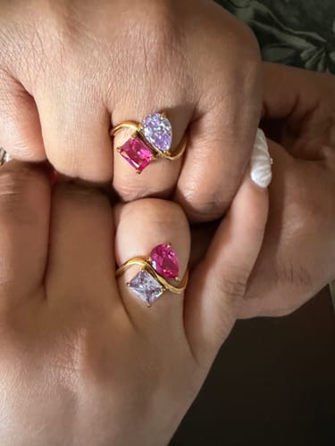 Reviewer shows two hands clasped, each wearing a Navae Birthstone Ring with pink and lavender stones.