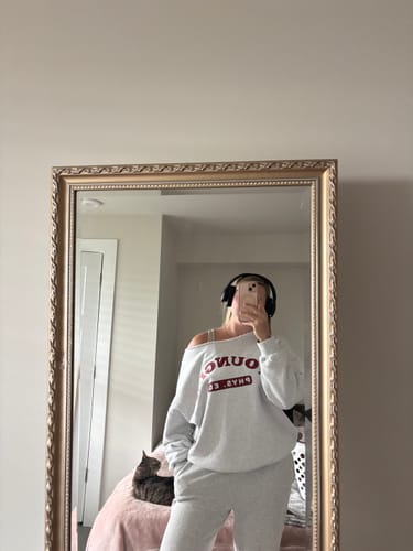 Reviewer taking a mirror selfie in a light grey, oversized P.E. Crewneck worn off-the-shoulder with matching pants.